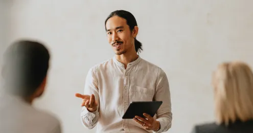 Junger Mann hält eine Präsentation mit einem Tablet und gestikuliert dabei.