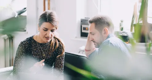 Zwei Personen sitzen in einem hellen Raum auf einem Sofa und scheinen in ein Gespräch vertieft zu sein.