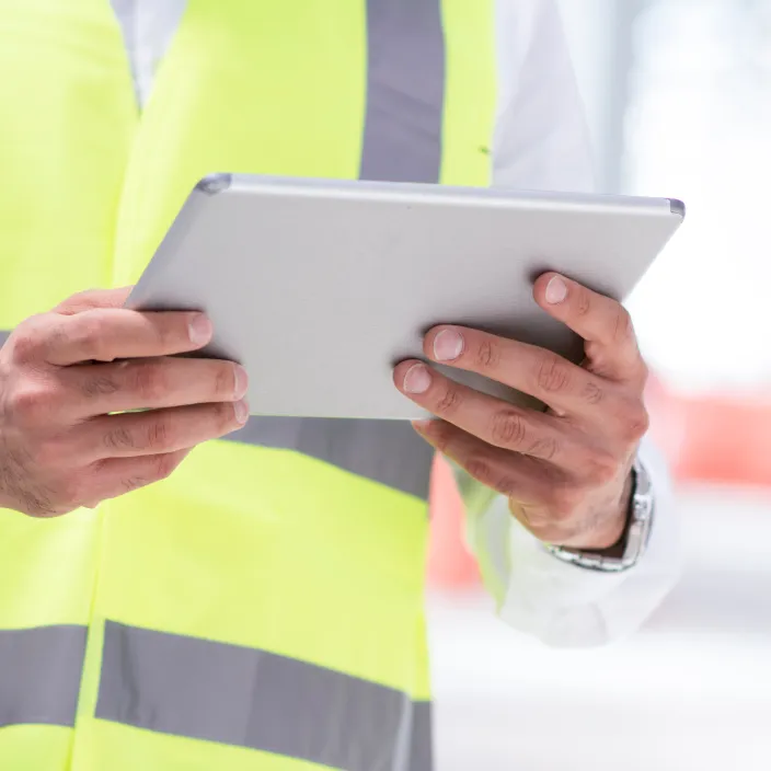 Ein Mann in einem hellblauen Hemd steht in einer modernen Fabrikumgebung und hält ein Tablet in der Hand.