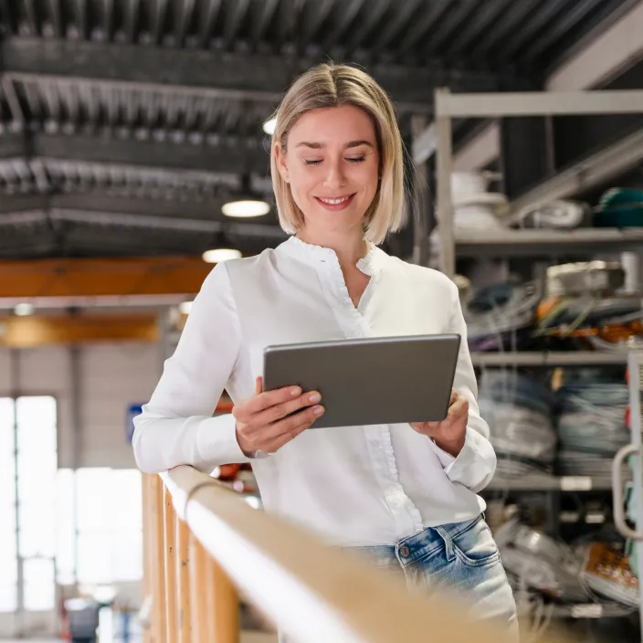 Ein Mann in einem hellblauen Hemd steht in einer modernen Fabrikumgebung und hält ein Tablet in der Hand.