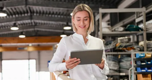 Ein Mann in einem hellblauen Hemd steht in einer modernen Fabrikumgebung und hält ein Tablet in der Hand.