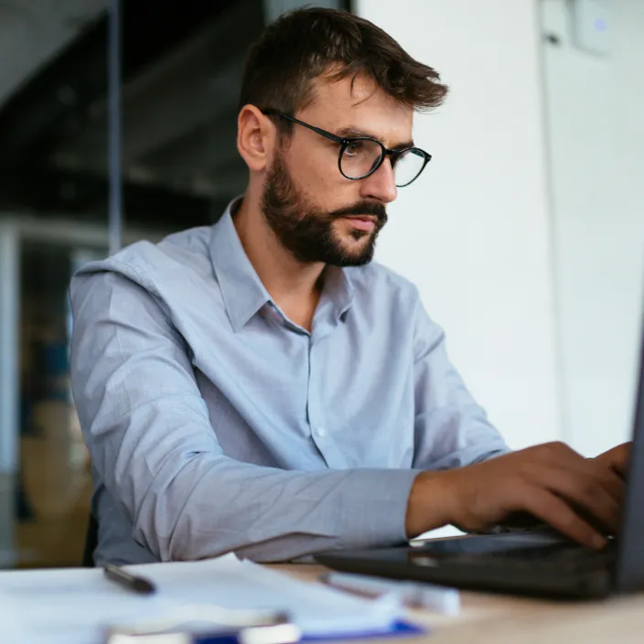 Ein Mann in einem hellblauen Hemd steht sitzt vor einem Arbeitsrechner.