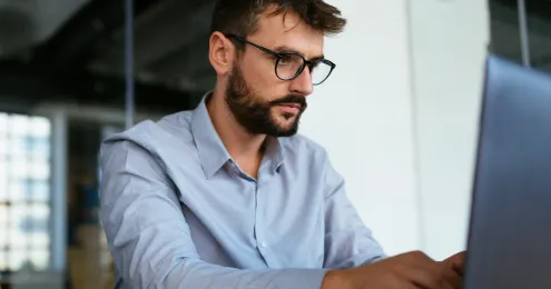 Ein Mann in einem hellblauen Hemd steht sitzt vor einem Arbeitsrechner.