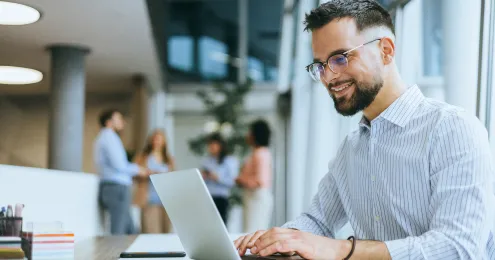 Ein Mann in einem Hemd arbeitet an einem Laptop, während er an einem Schreibtisch sitzt