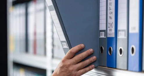 Eine Person greift nach einem Ordner in einem Aktenschrank