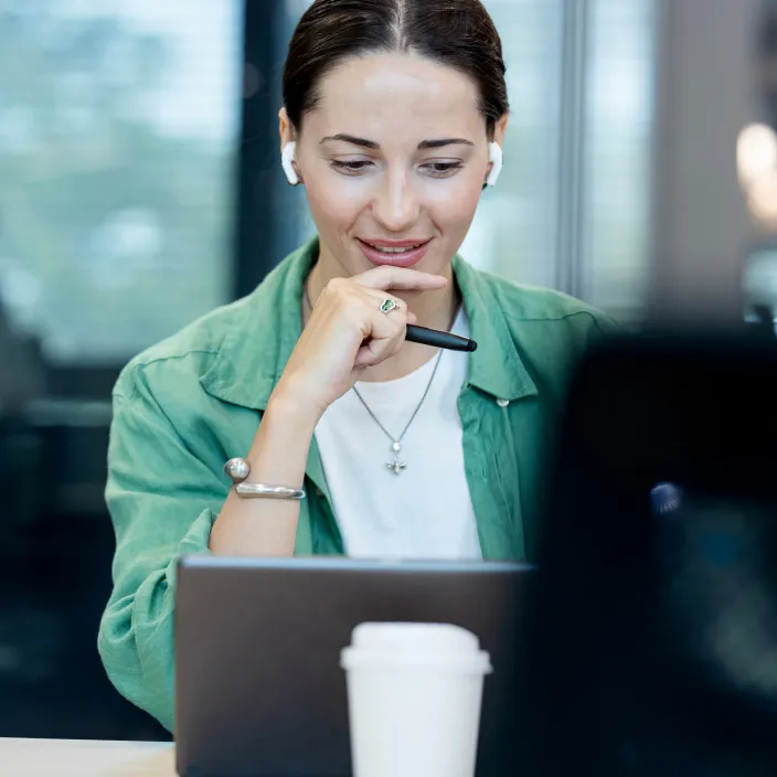Person in einem modernen Büro, die konzentriert an einem Laptop arbeitet, mit einer Kaffeetasse im Vordergrund