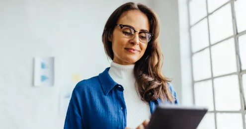 Frau mit Brille hält ein Tablet in einem hellen Büro.