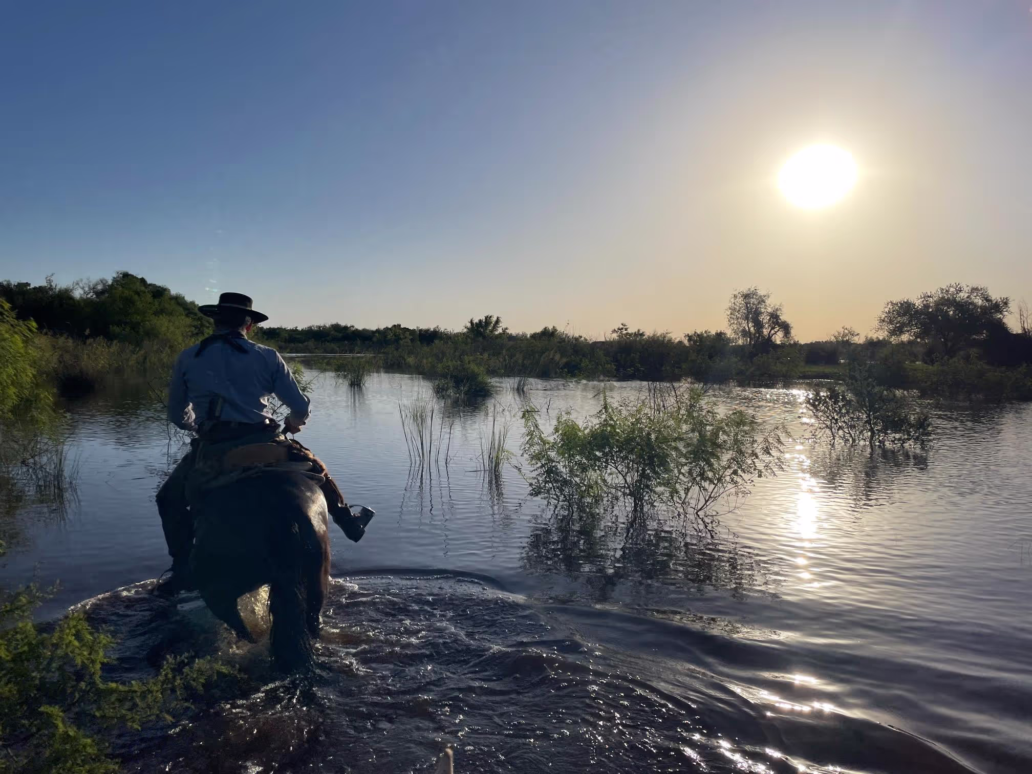Horse and rider crossing a large river at sunset