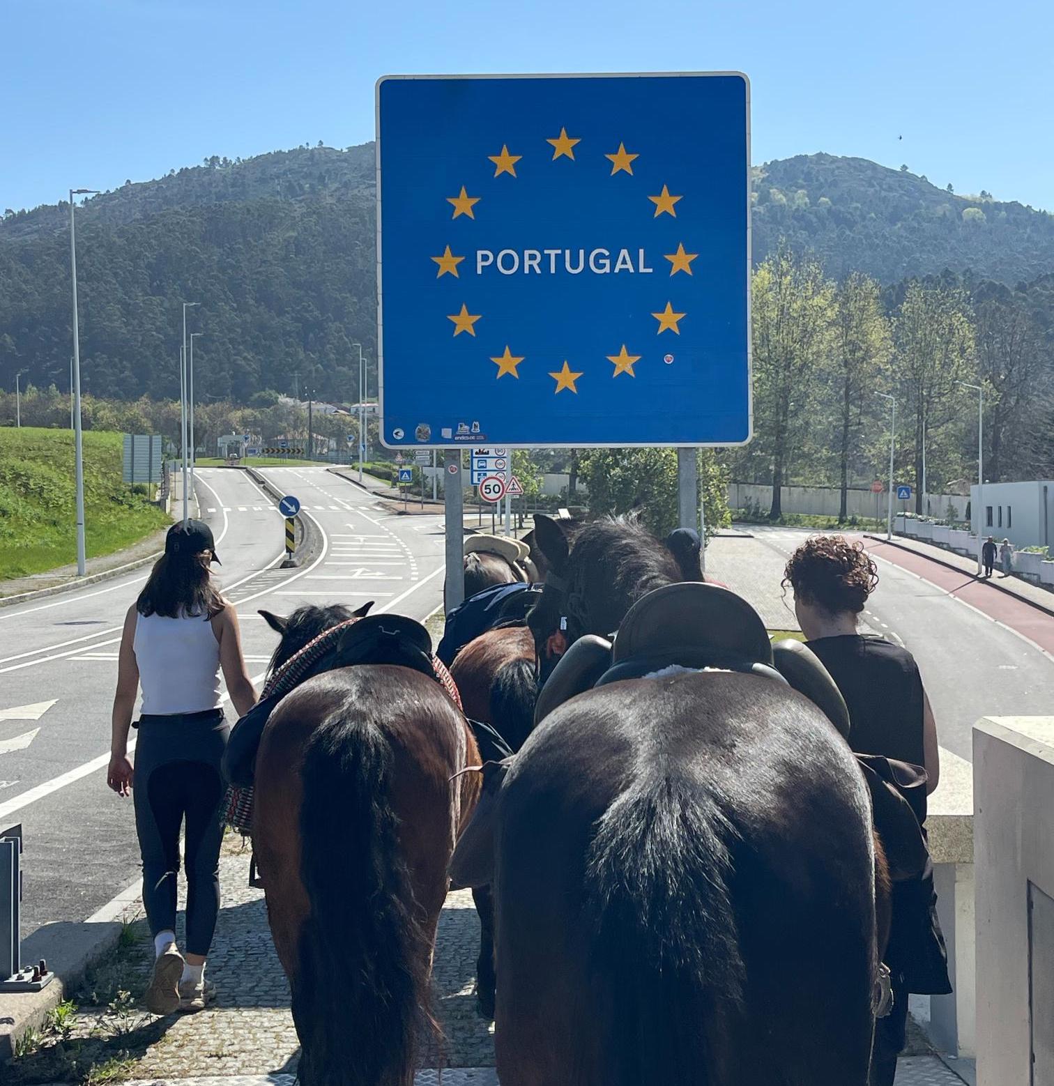 Horses and riders walking across the border of Portugal just in front of the sign 