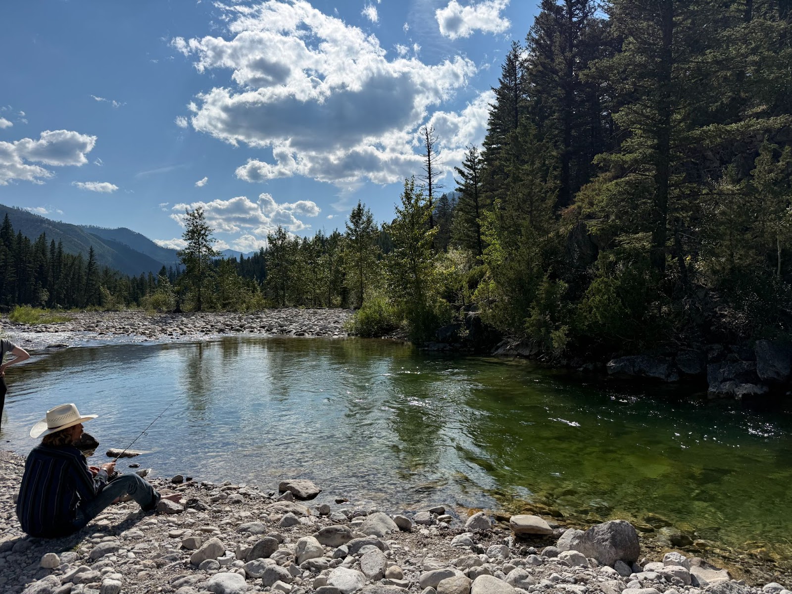 Cowboy fishing at a river in the forest surrounded by mountains