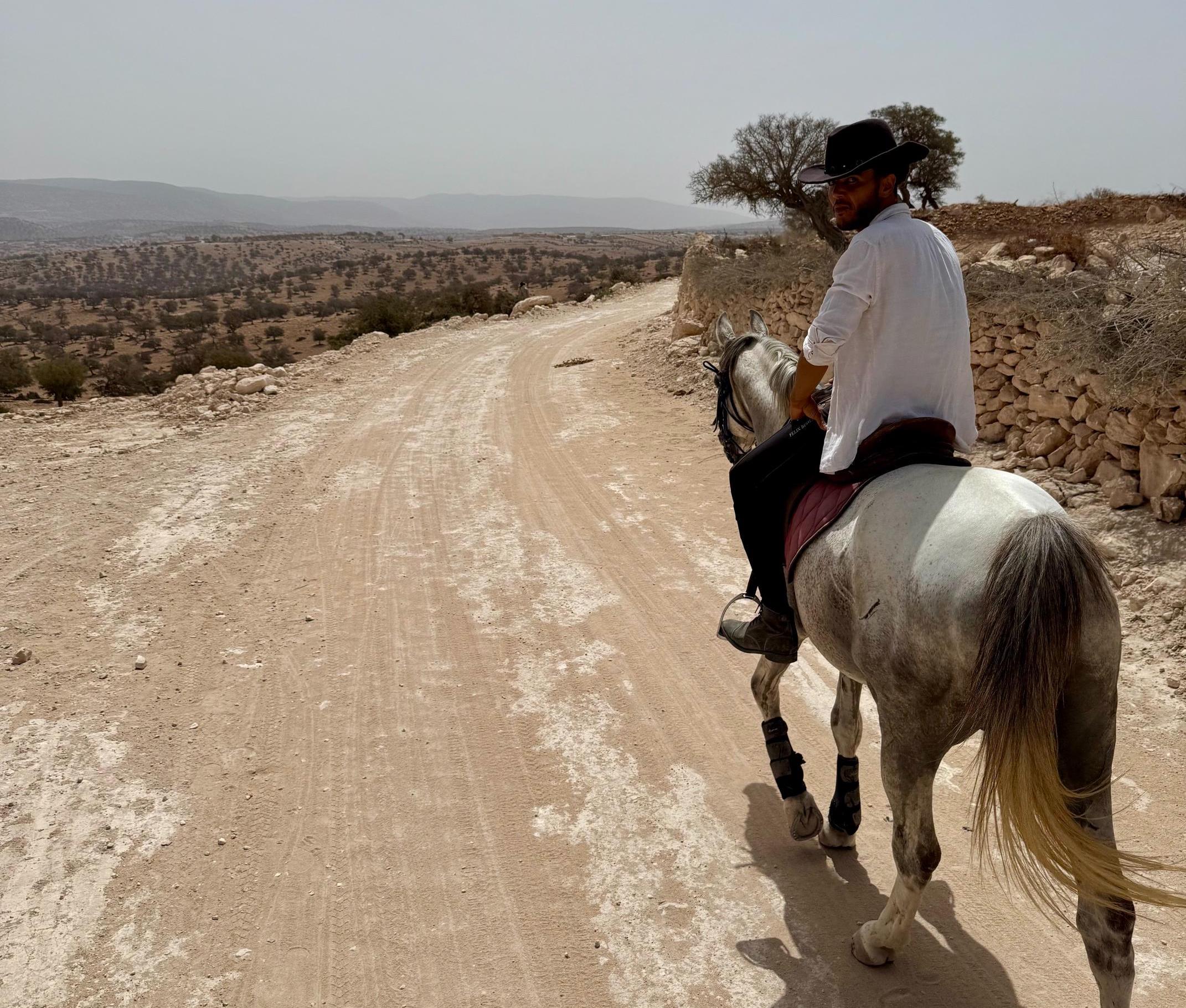 Man on grey horse walking along a dirtroad in the desert