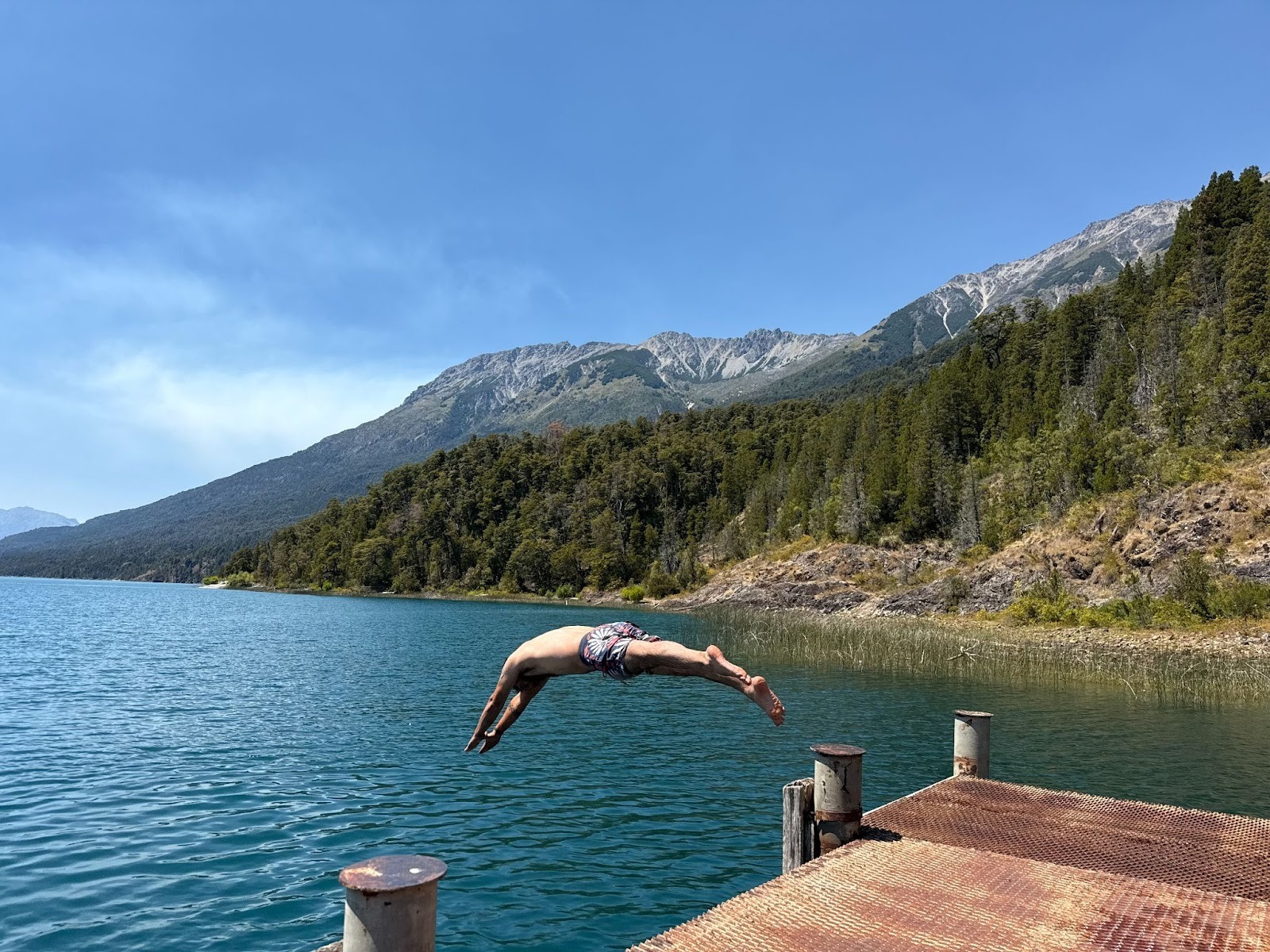 Man diving from the dock into the lake in the middle of the mountains