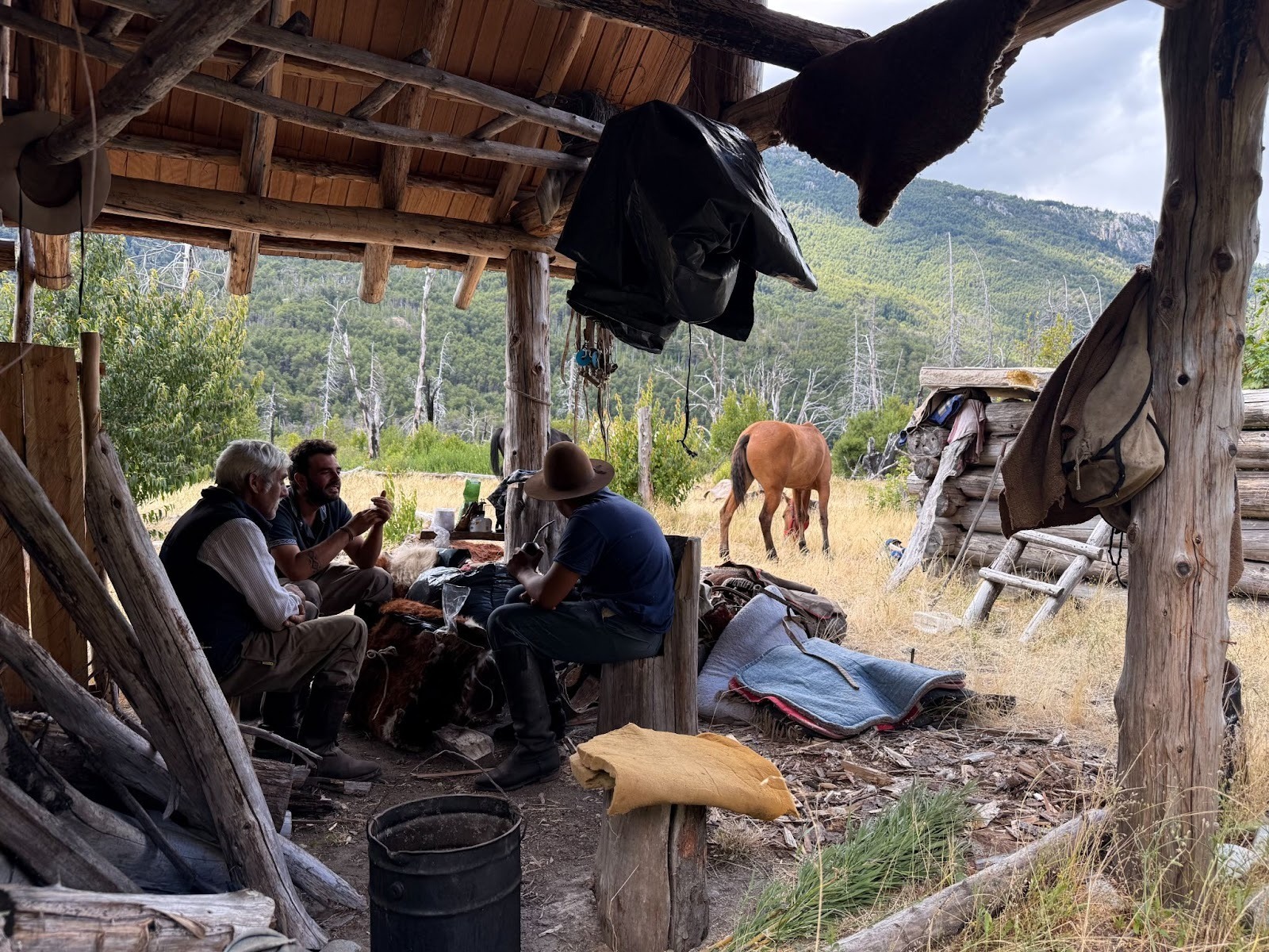Gauchos drinking mate in front of a cabin while looking at the horses