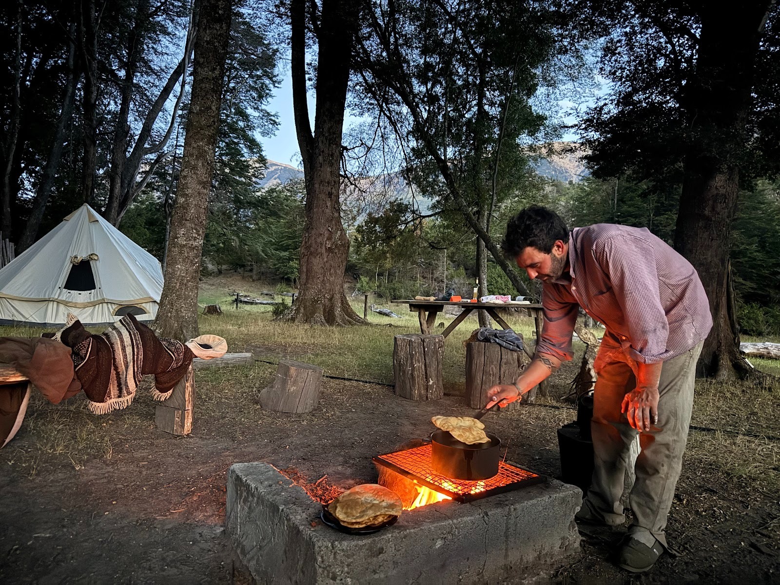 Gaucho cooking over the fire at a tented camp in the forest, surrounded by mountains