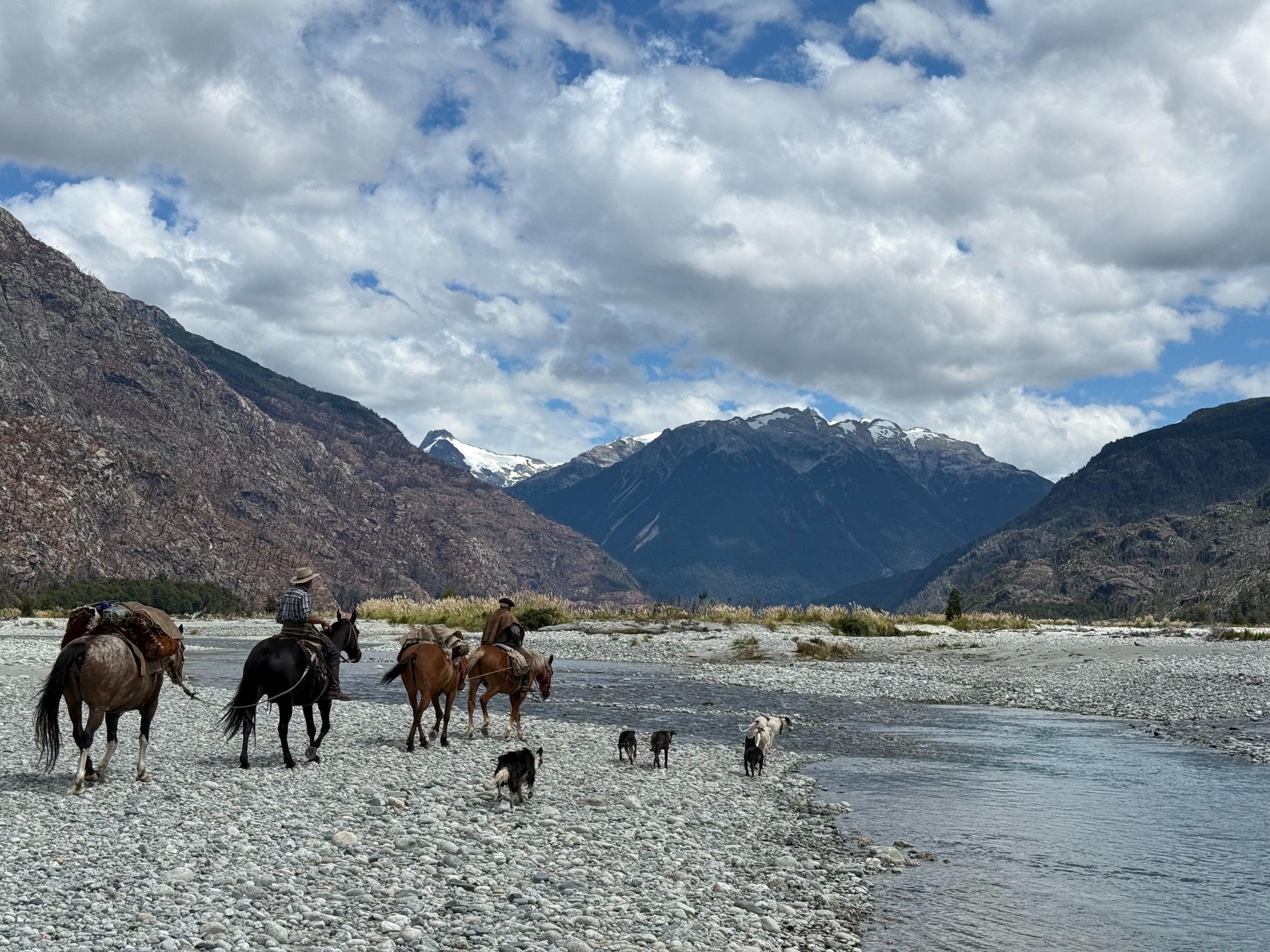Horses and riders walking across river surrounded by mountains