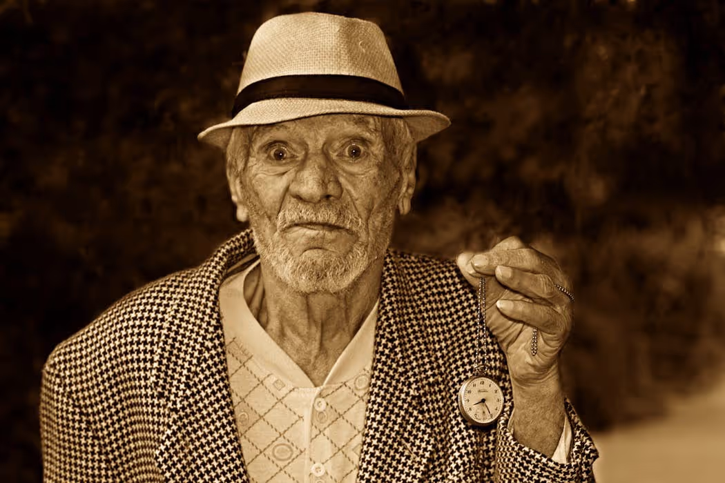 Un portrait sépia d'un homme âgé tenant une montre à gousset, vêtu d'un chapeau de paille et d'une veste à motifs houndstooth, incarnant la sagesse et la nostalgie d'une époque révolue.