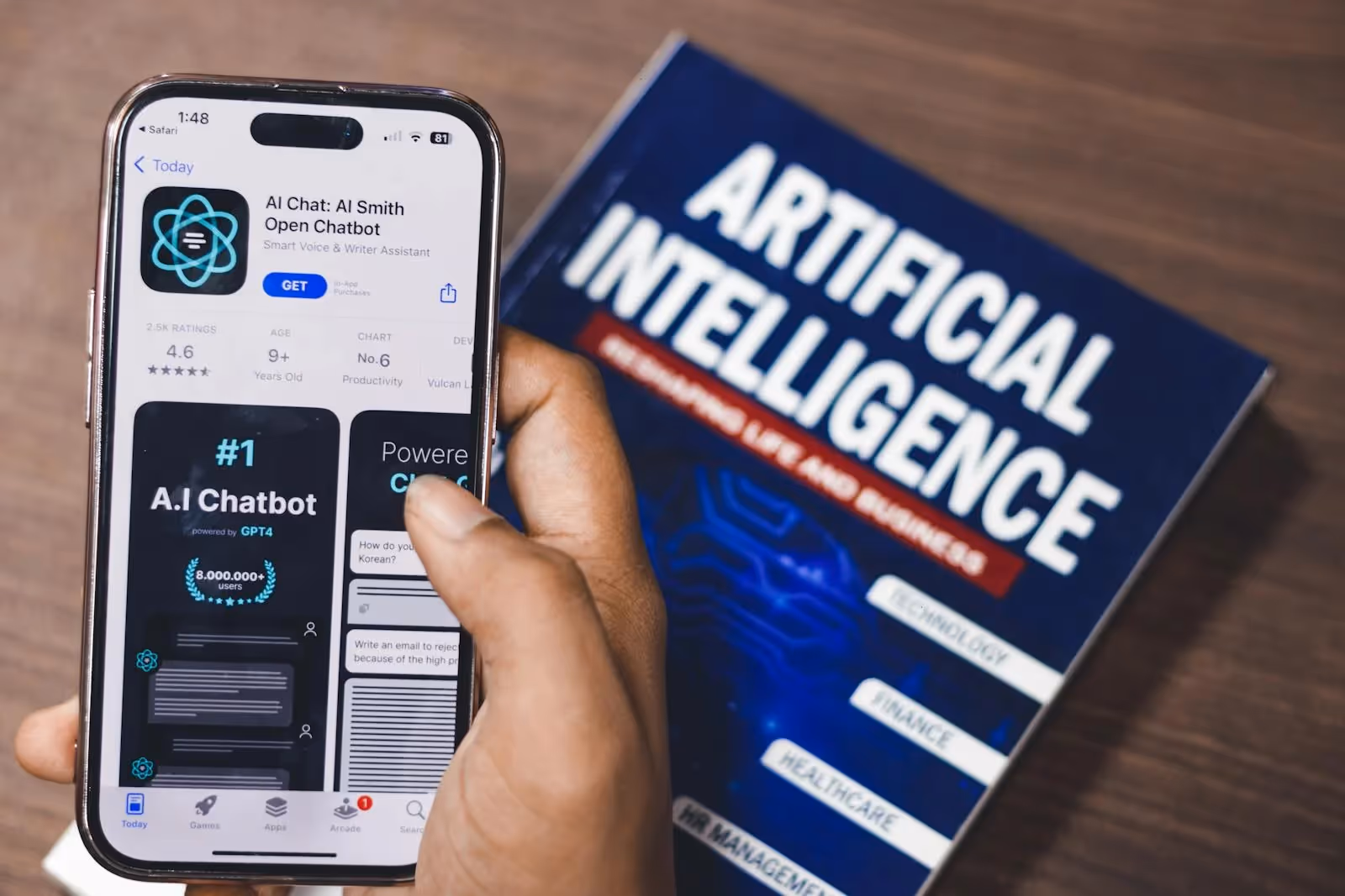 Une personne qui tient un téléphone avec l'interface de l'application d'une app IA et on voit au fond un livre sur l'intelligence artificielle.