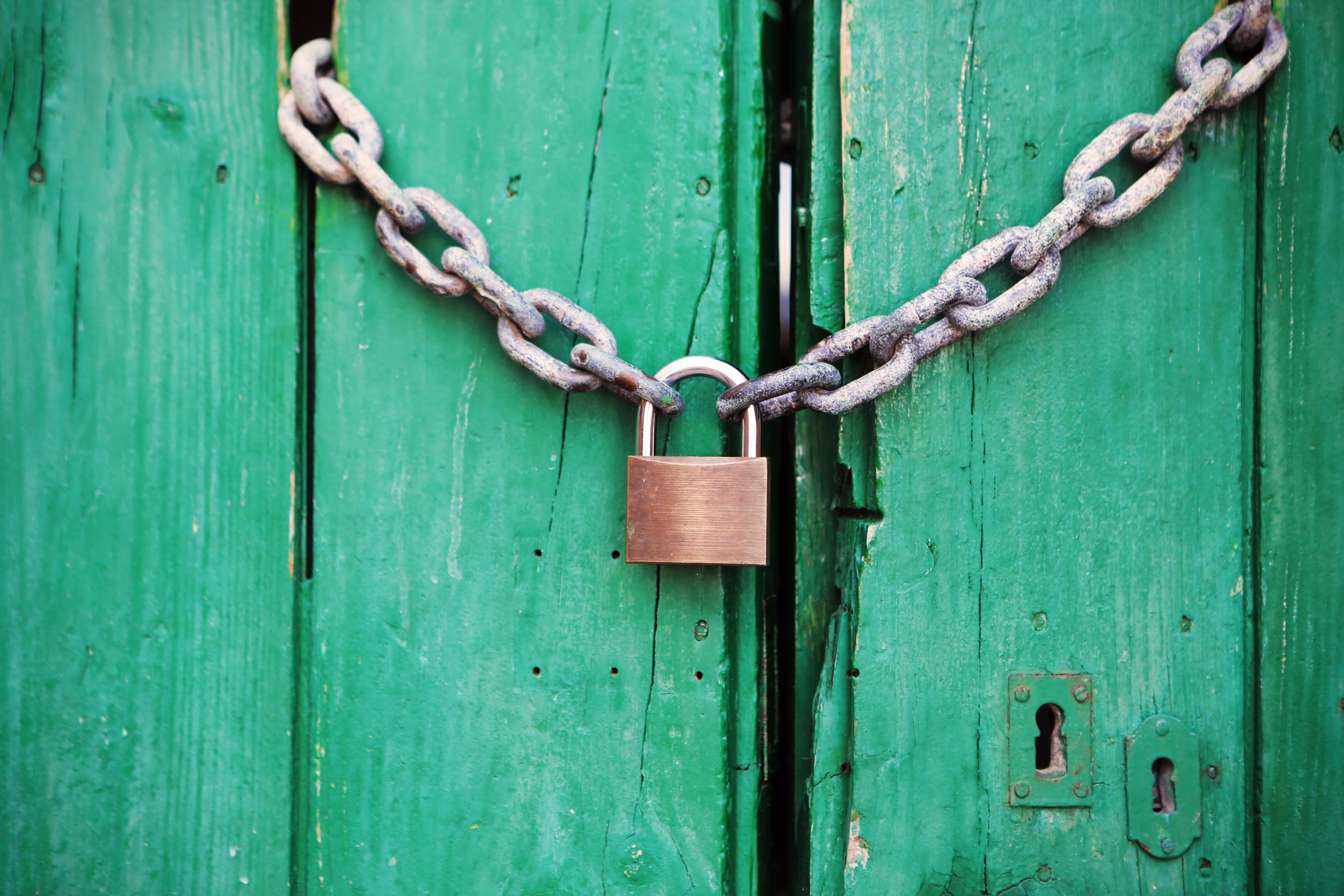 Cadenas en métal fixé sur une chaîne rouillée, verrouillant deux portes en bois peintes en vert vif — symbolisant la sécurité et la protection des accès.