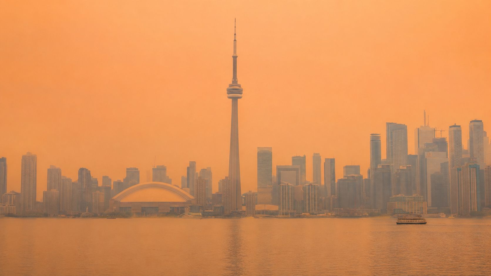 The Toronto skyline shrouded in a thick, orange haze from wildfire smoke viewed across Lake Ontario.