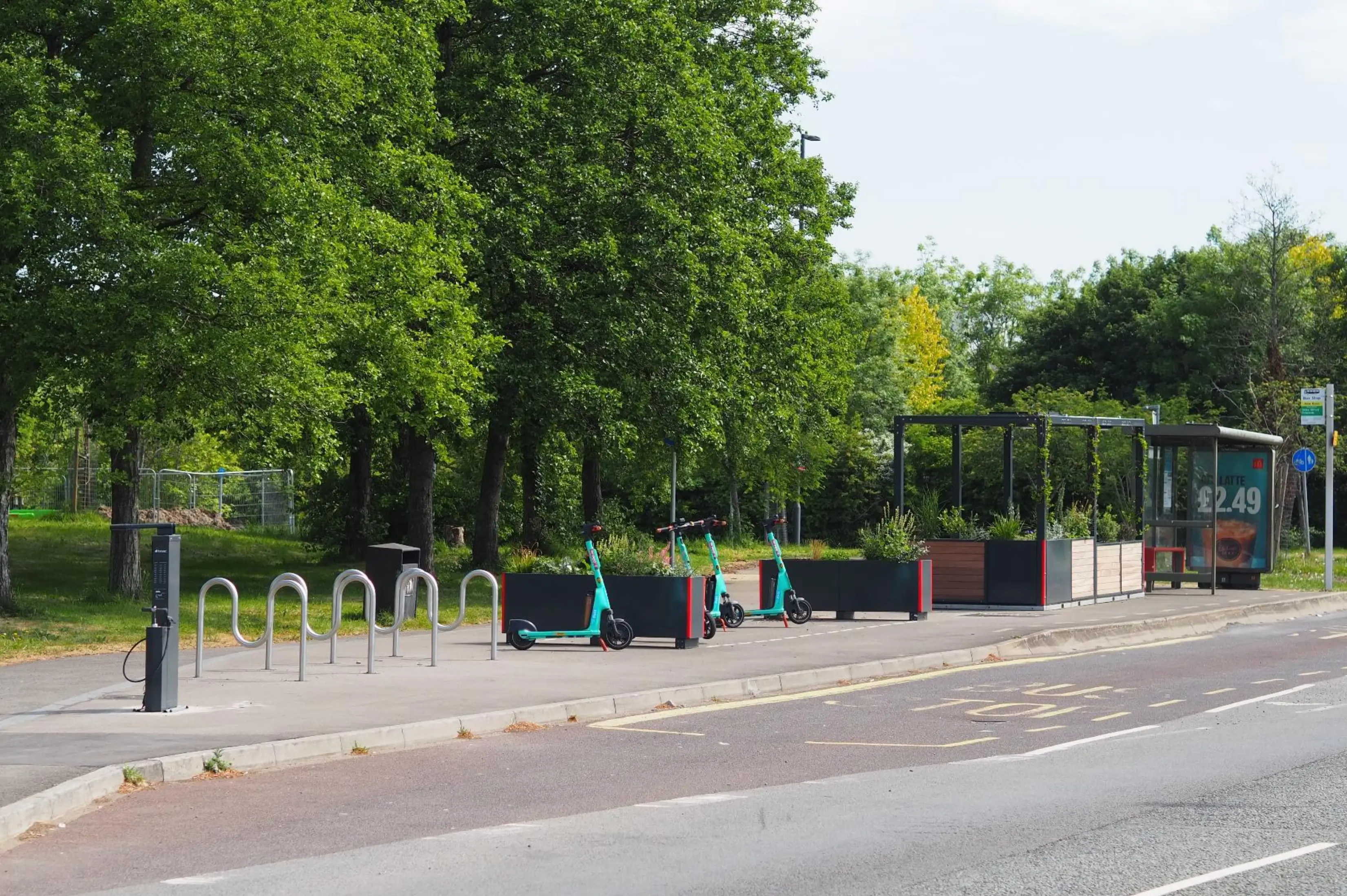 Abbey Wood Shopping Park mobility hub with bike racks, shared e-scooters, planters and a sheltered bus stop