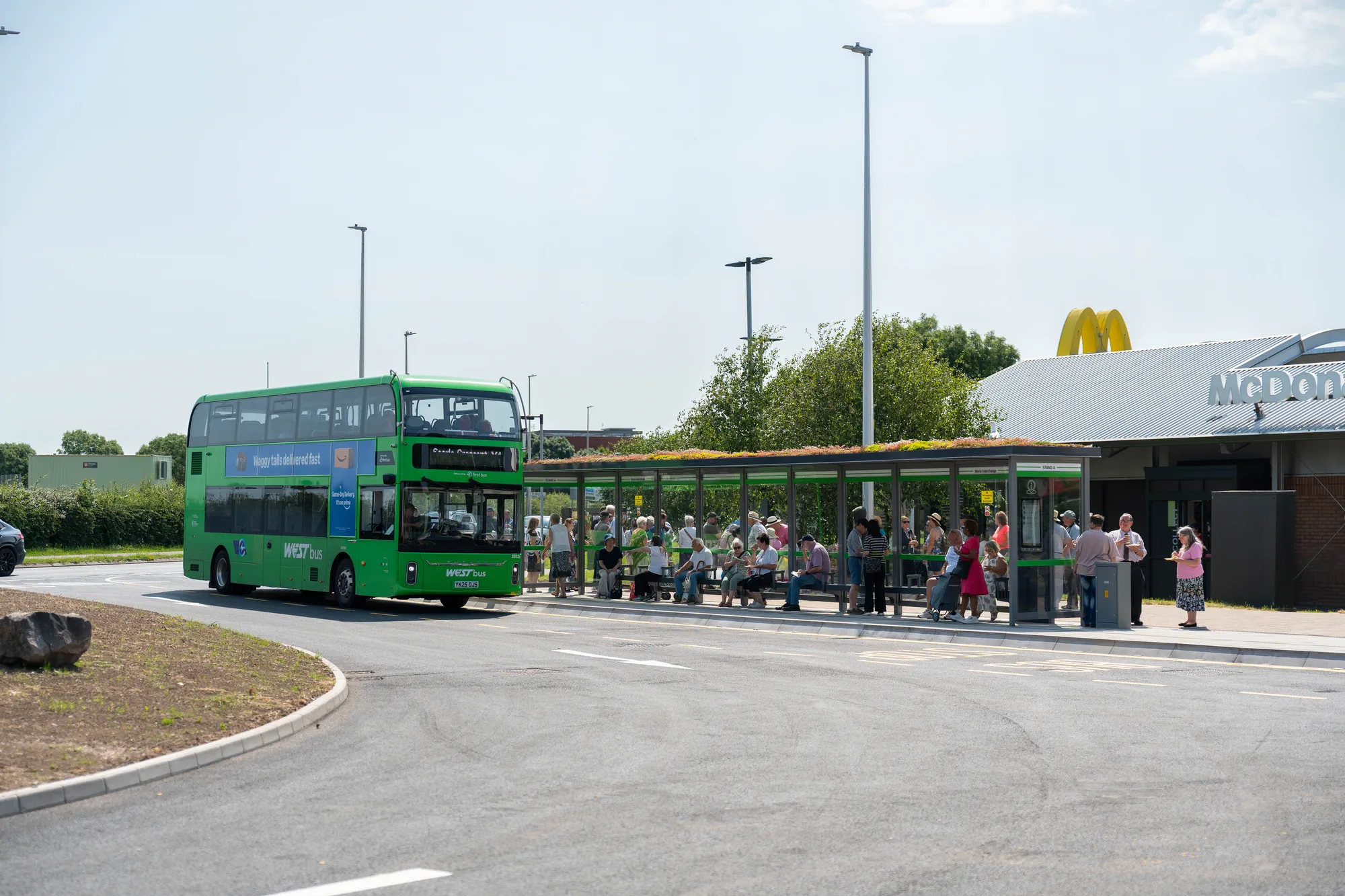 Green double-decker WEST bus pulling up to a crowded shelter at Worle Interchange.
