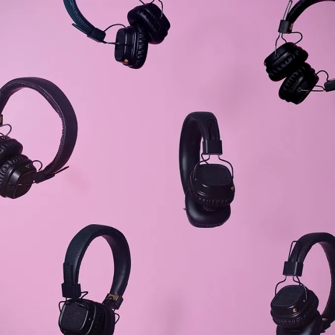 Multiple black over-ear headphones arranged against a solid pink background.