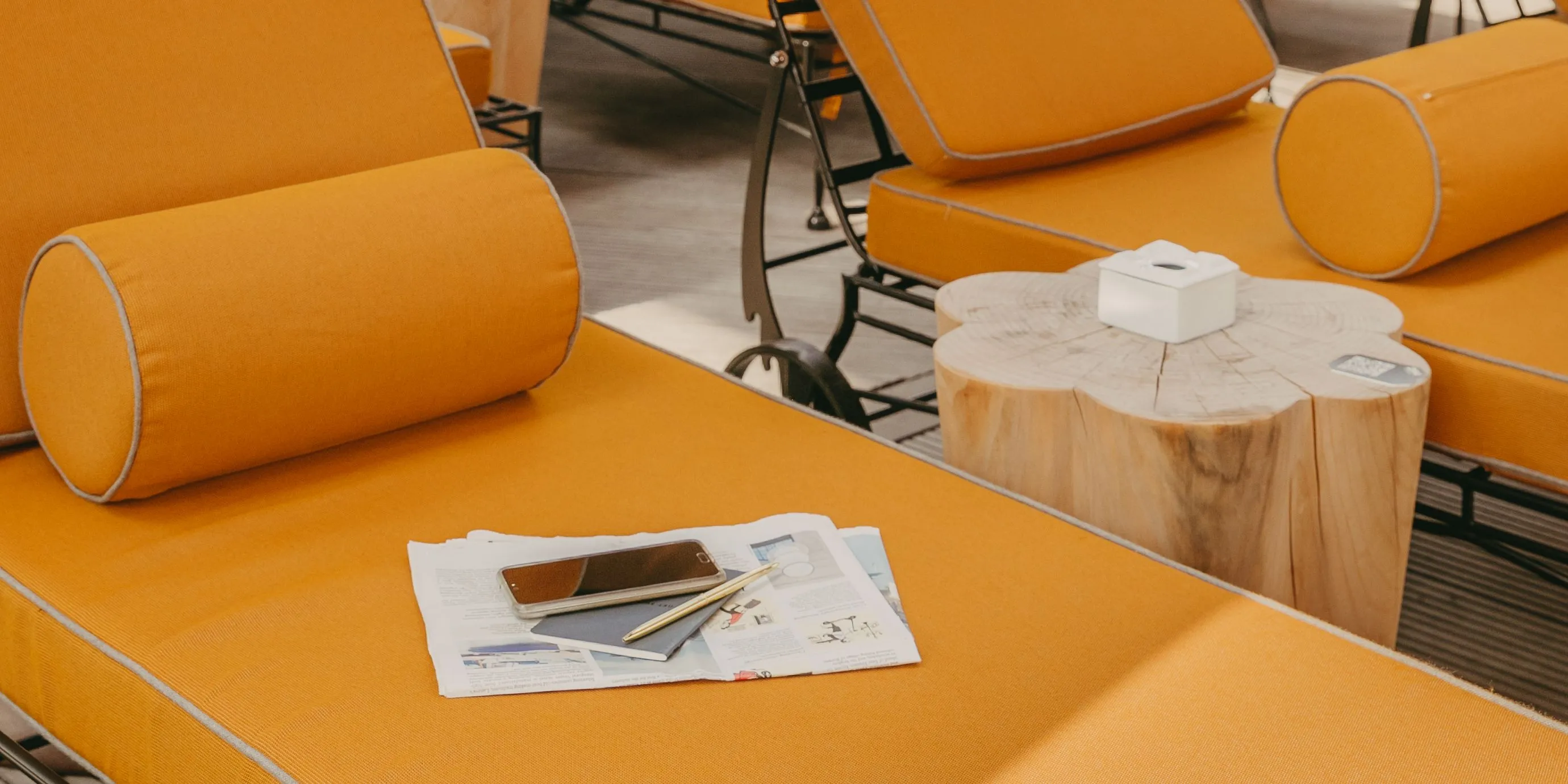 Photo of orange lounge chairs with a magazine, phone, and glasses next to a wooden side table with a tissue box.