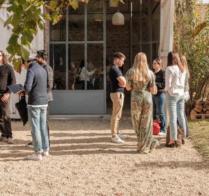 Photo of a group of people chatting outside a building, surrounded by trees.