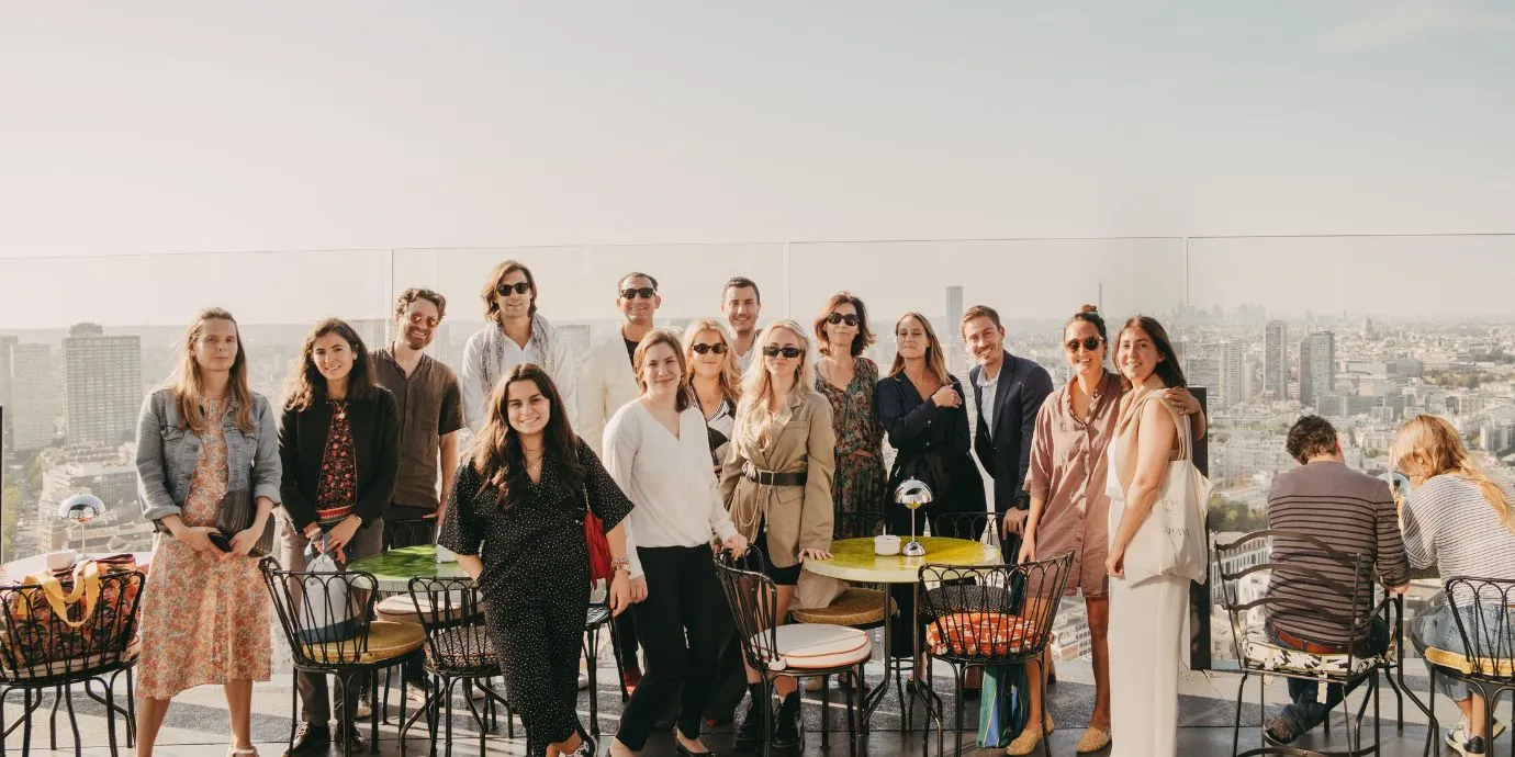 A group of fifteen people standing and sitting on a rooftop terrace with city skyline in the background on a sunny day.