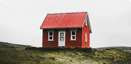 Small red cabin with a red roof standing alone on green grassy land under a gray sky.