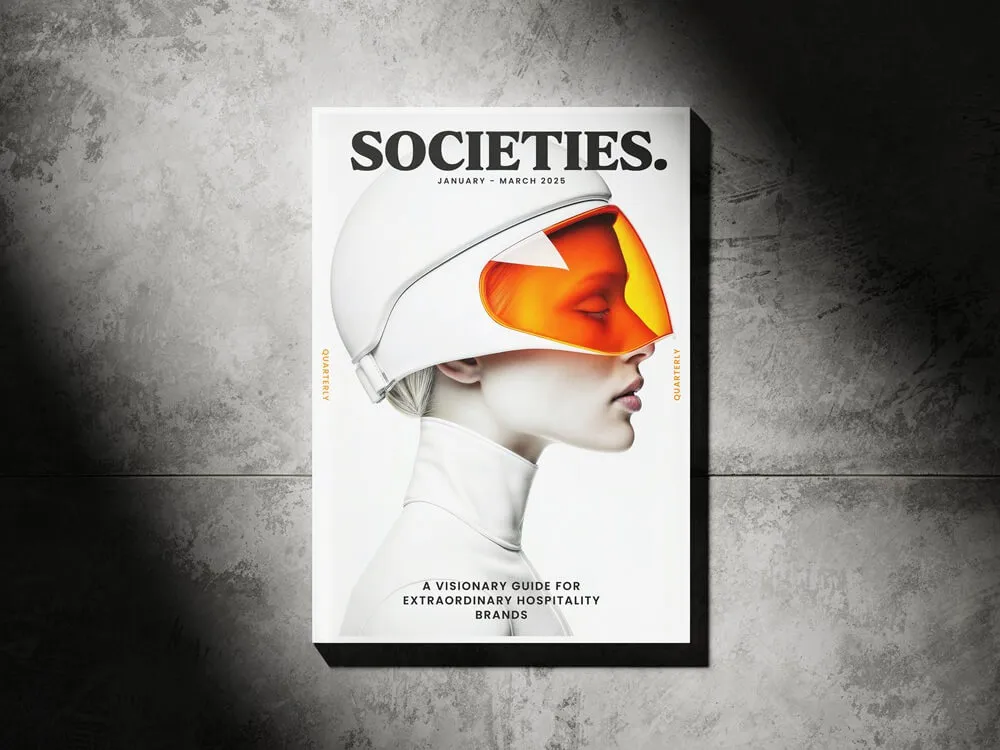 Magazine cover titled 'SOCIETIES.' with a profile image of a person wearing a white helmet with an orange visor, subtitled 'A visionary guide for extraordinary hospitality brands'.