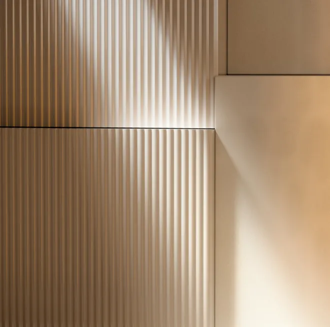 Close-up of a beige wall with vertical ridges and smooth panel sections illuminated by soft angled lighting.