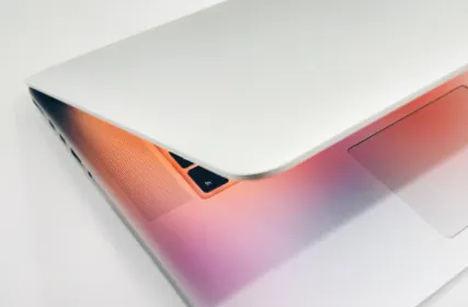 Partially closed silver laptop with an orange backlit keyboard on a white surface.