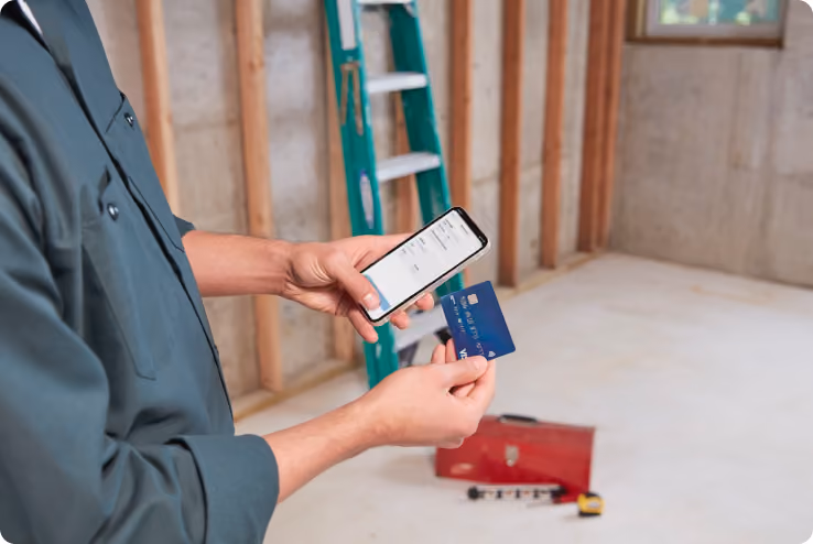 Small business owner in a customer's home, holding an iPhone and a credit card