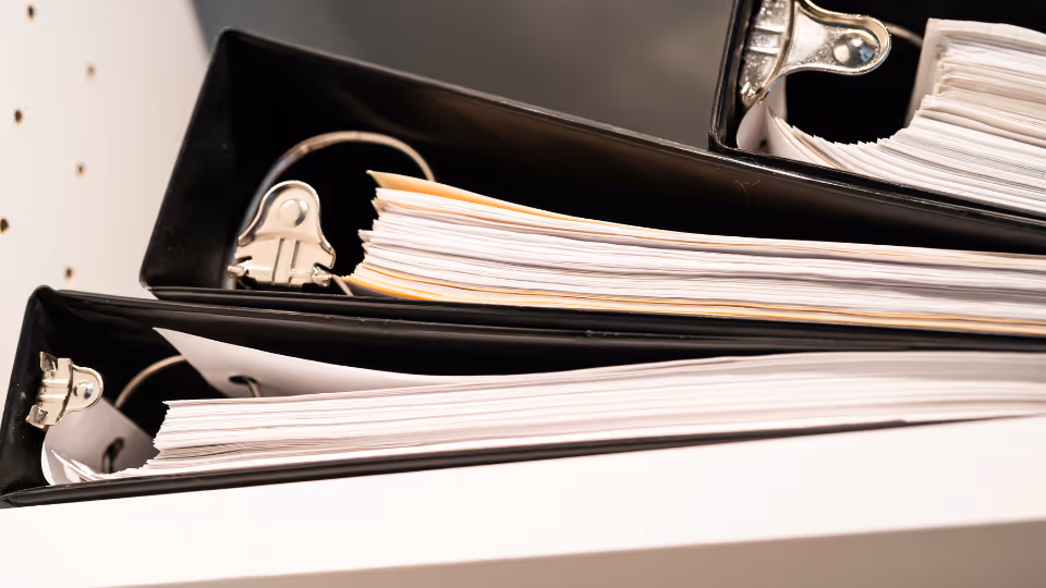 A stack of binder files on top of a desk