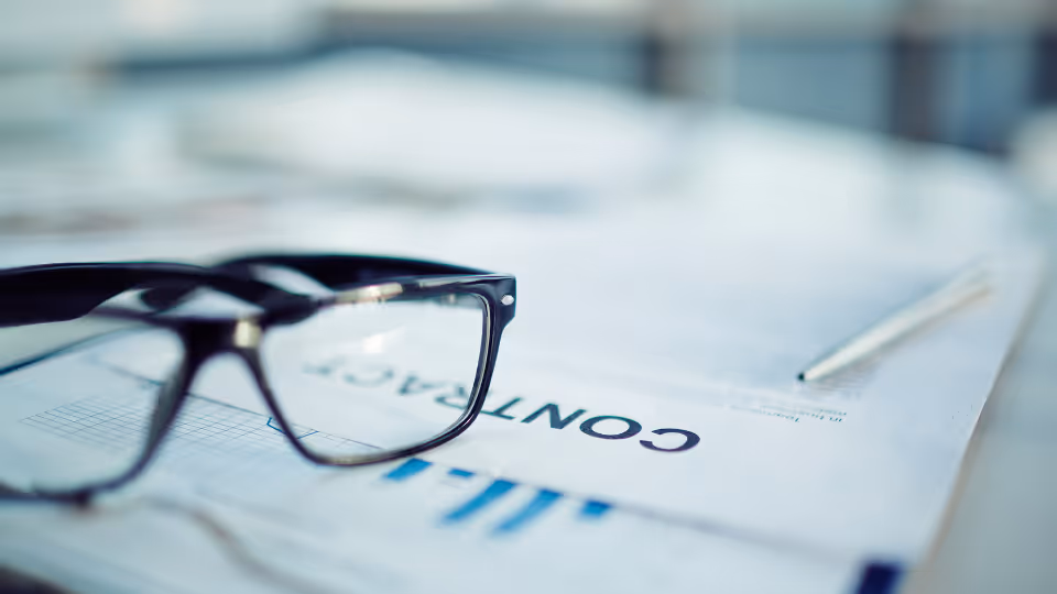 Alt text: Glasses sitting on a contract on a conference table