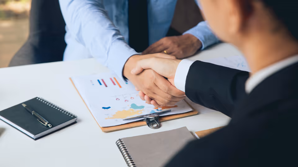 Two business people shaking hands at a desk