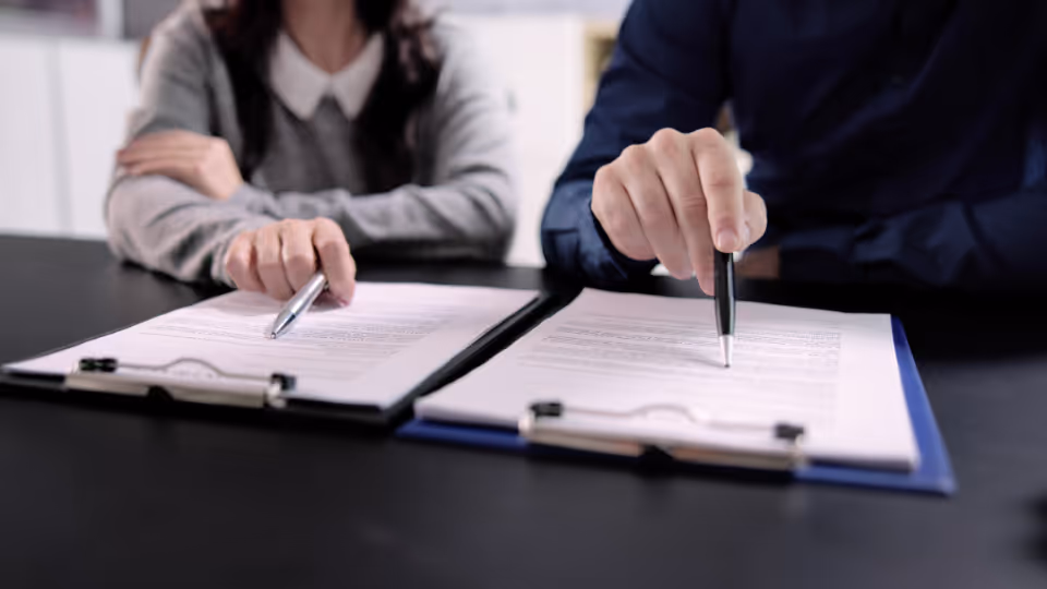 Alt text: Two people sitting at a table with papers and pens