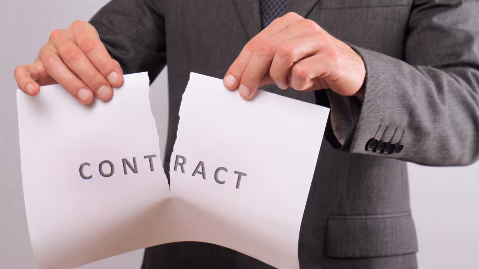 Alt text: A person in a suit tearing up a piece of paper with the word contract written on it