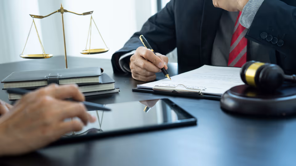 Alt text: A person in a suit sitting at a desk with a tablet and a scale of justice in front of them