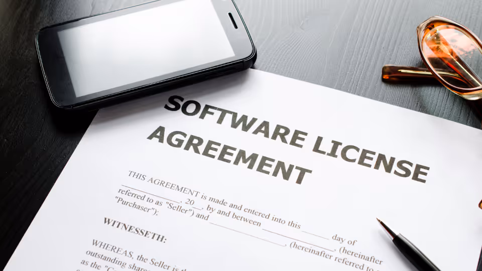 Alt text: A close up of a Software License Agreement on a desk with a cellphone and a pair of glasses