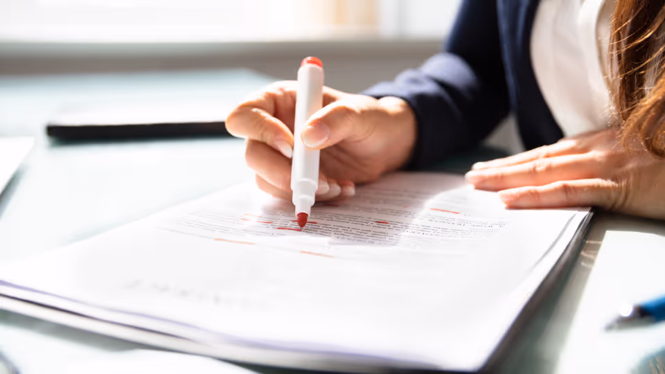 Alt text: A person using a red marker to make the first round of edits on a contract