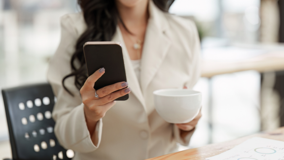 A person in a business suit holding a cup and looking at their phone