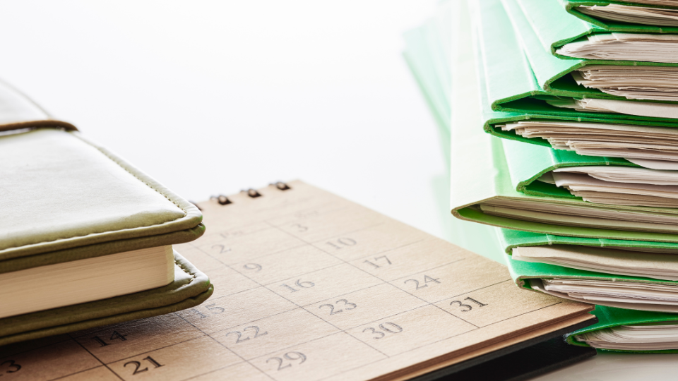 Alt text: A stack of contracts beside a calendar for tracking deadlines