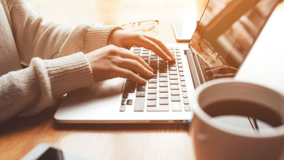 Alt text: A person drafting a contract on a laptop with a cup of coffee