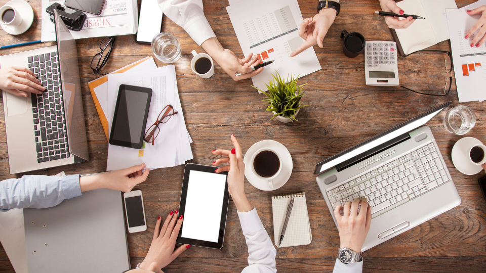 Alt text: A team of people sitting around a table with laptops and papers