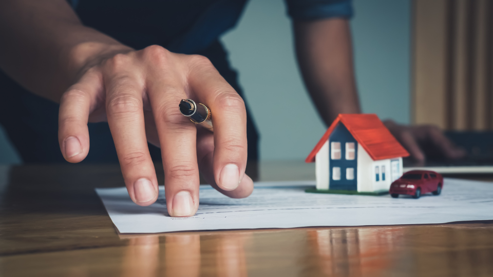 A real estate agent signing a contract with a small model house placed on top of the document