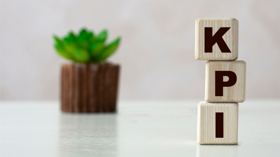 Alt text: Wooden blocks spelling KPI in front of a potted plant on a desk