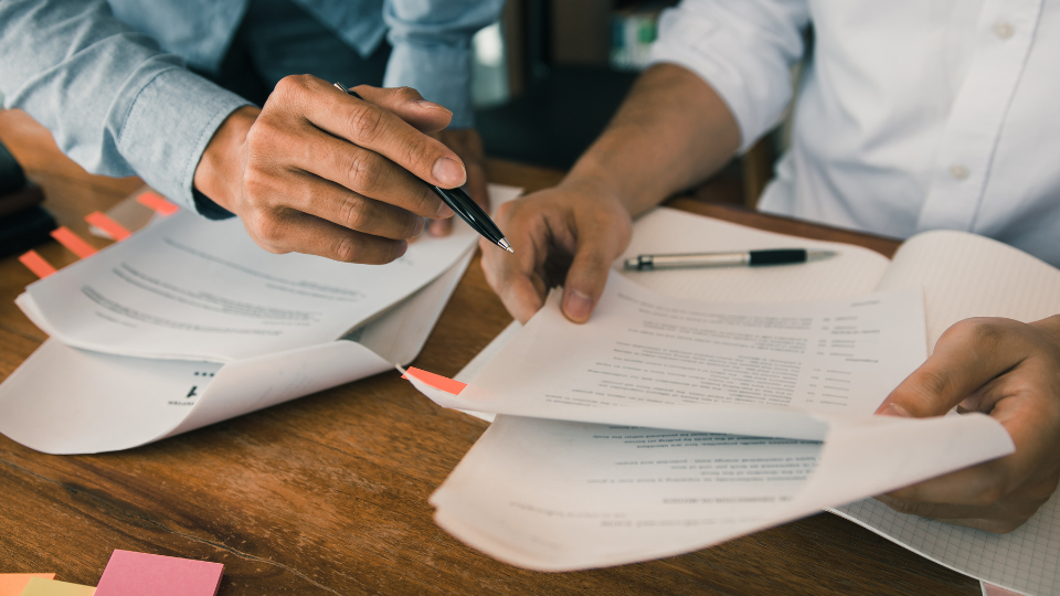 Two people reviewing a contract together at a desk, with pens and sticky notes