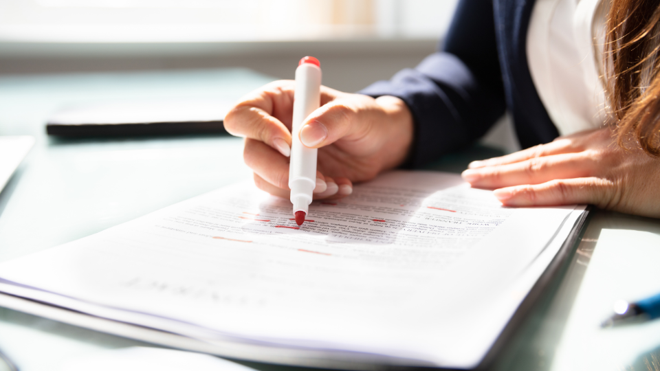 Alt text: A person using a red marker to make the first round of edits on a contract